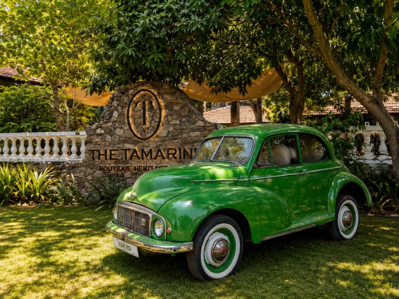 Vintage car beside The Tamarind stone wall and logo